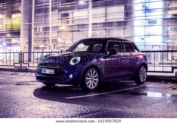 17 January 2020 Mini Cooper S John Works stands on\
Parking slot at night , front view. Background modern glass house\
house. After rain mood. 