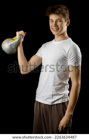 A 17 year olf teen boy lifing a kettlebell against a black background