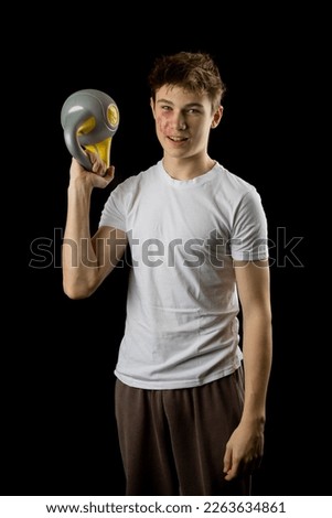 A 17 year olf teen boy lifing a kettlebell against a black background