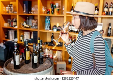 18 OCTOBER 2018, TUSCANY, ITALY: 
 Happy Asian Woman Sniffing And Tasting Red Wine In A Glass In Winery Shop