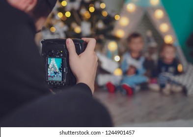 18.11.2018 Vinnitsa, Ukrine: Photographer Who Works And Photographs Children In A Thematic Photo Studio Adorned To Christmas And New Year. A Man With A Camera Photographs A Baby At Home,