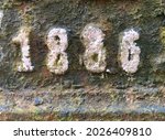 "1886" taken from a cast-iron inscription produced that year. Corroded and painted in white, covered with lichen in different colours