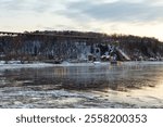 The 1908 railway trestle bridge and houses along the Chemin de la Plage Jacques-Cartier seen with their reflection in the St. Lawrence river during a cloudy winter dawn, Quebec City, Quebec, Canada