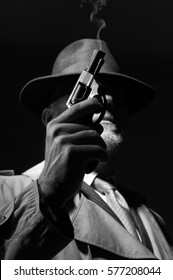 1950s Style Detective Posing In The Dark, He Is Holding A Weapon And Wearing A Fedora Hat, Noir Film Character