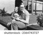 1978 vintage, seventies, retro roll film monochrome portrait of father and daughter sitting in front of a house in the summer sun.	