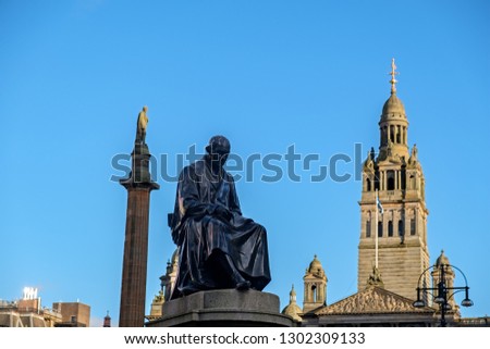 A 19.c. Statue of James Watt (inventor of the steam engine) with the column of Sir Walter Scott and Glasgow City Chambers at the background. Glasgow, Scotland