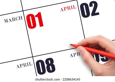 1st Day Of April. A Hand Holding A Red Pen And Pointing On The Calendar Date April 1. Red Calendar Date, Copy Space, Mockup. Spring Month, Day Of The Year Concept.