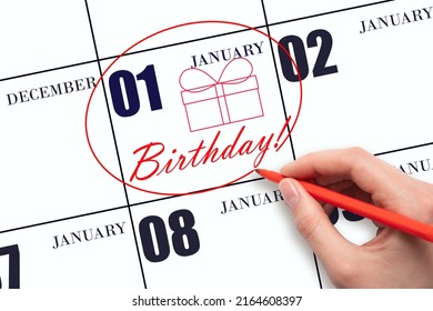 1st Day Of January. The Hand Circles The Date On The Calendar 1 January, Draws A Gift Box And Writes The Text Birthday. Holiday. Winter Month, Day Of The Year Concept.