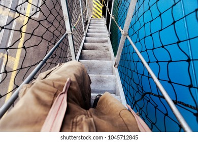 1st Person View Of Legs Walking Down A Flight Of Stairs Connecting A Freighter Ship And The Dock.