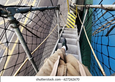 1st Person View Of Legs Walking Down A Flight Of Stairs Connecting A Freighter Ship And The Dock.