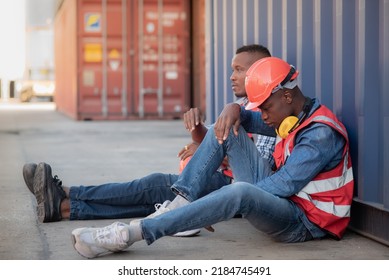 2 African lack man worker wearing safety uniform workwear and sitting on the floor leaning against the container, there is stressed and no work to do, economic recession due to inflation. - Shutterstock ID 2184745491