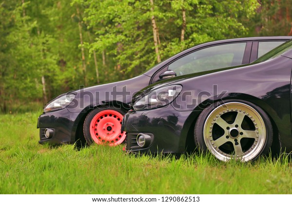 2 black cars in tuning.\
Parked on grass. With custom polished wheels, and living coral\
color wheel.
