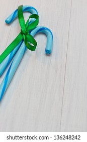 2 Blue Candy Canes Tied With Green Ribbon On Distressed White Wood