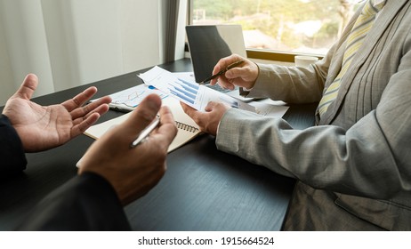 2 Business People Meeting In The Office Who Discuss Company Success With Graphs And Laptop On The Table.