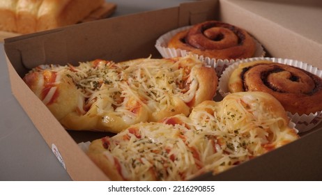 2 Cinnamon Rolls And 2 Sausage Rolls With Cheese And Souse On Top In A Paper Container.