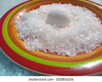 2 Different Textures Of Salt Refined Salt And Coarse Salt Concentrated Inside And Outside A Saucer Of Bolivian Origin, Handmade In Yellow, Red And Orange Colors On A Smooth White Surface