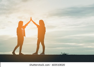 2 friends hand  giving high five to congratulate the achievement against the sunset background