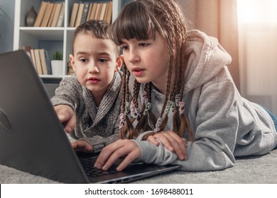 2 Kinder, Mädchen und Junge, surfen im Internet auf einem Laptop, der zu Hause auf dem Boden liegt, während der Quarantäne