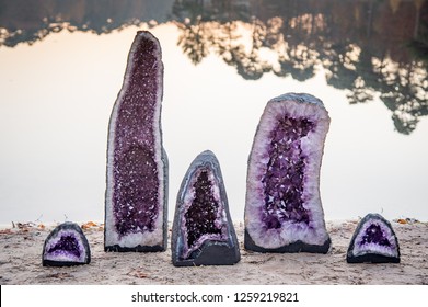 2 large and 3 small amethyst crystal geodes near the water of a lake during sunset