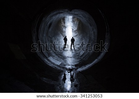 2 men in dark underground pipe with light peering in