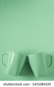 2 Monochromatic Green Coffee Mugs On Green Background Clinking In Cheers With Blank Empty Room Space For Text, Copy, Or Copyspace. Modern Top View Concept Of Two Cups With Solid Background Backdrop.