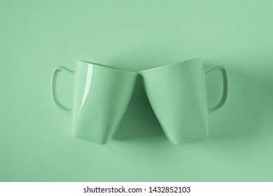 2 Monochromatic Green Coffee Mugs On Green Background Clinking In Cheers With Blank Empty Room Space For Text, Copy, Or Copyspace. Modern Top View Concept Of Two Cups With Solid Background Backdrop.