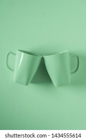 2 Monochromatic Green Coffee Mugs On Green Background Clinking In Cheers With Blank Empty Room Space For Text, Copy, Or Copyspace. Modern Top View Concept Of Two Cups With Solid Background Backdrop.