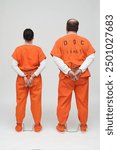 2 prisoners in handcuffs and leg irons with belly chain and orange overalls, back view