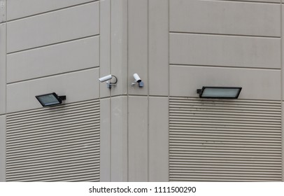 2 security cameras on the side of a building with 2 lights