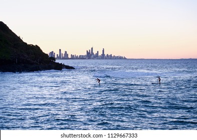 2 SUP Stand Up Paddle Boarders enter the inlet of Tallebudgeera Creek, Gold Coast, Australia on a winter evening. Surfers Paradise sits in silhouette on the horizon, Burleigh Heads in shadow,