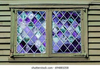 2 vintage windows with purple panes in a leaded diamond pattern on a colonial building