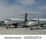 2 white, blue, and gold private jets parked at an airport