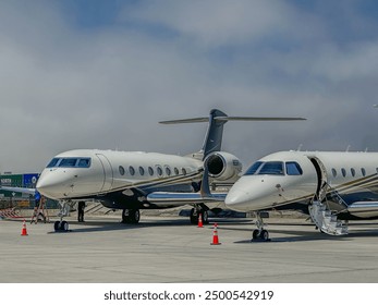 2 white, blue, and gold private jets parked at an airport - Powered by Shutterstock