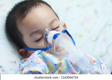 2 Years Old Asian Toddler Boy Has Asthma Or Pneumonia Disease And Need Nebulizations,Sick Boy Rest On Patien Bed And Has Inhalation Therapy By The Mask Of Inhaler.Sick Or Cancer Child Awareness.