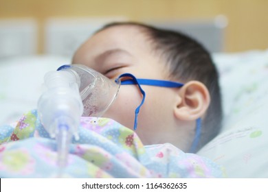 2 Years Old Asian Toddler Boy Has Asthma Or Pneumonia Disease And Need Nebulizations,Sick Boy Rest On Patien Bed And Has Inhalation Therapy By The Mask Of Inhaler.Sick Or Cancer Child Awareness.