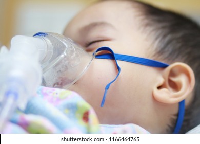 2 Years Old Asian Toddler Boy Has Asthma Or Pneumonia Disease And Need Nebulizations,Sick Boy Rest On Patien Bed And Has Inhalation Therapy By The Mask Of Inhaler.Sick Or Cancer Child Awareness.