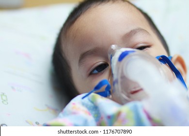 2 Years Old Asian Toddler Boy Has Asthma Or Pneumonia Disease And Need Nebulizations,Sick Boy Rest On Patient Bed And Has Inhalation Therapy By The Mask Of Inhaler.Sick Or Cancer Child Awareness.