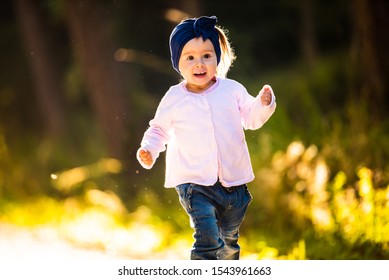 2 Years Old Baby Girl Running In Forest Towards Camera. With Happy Expression On Her Face