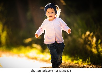 2 Years Old Baby Girl Running In Forest Towards Camera. With Happy Expression On Her Face