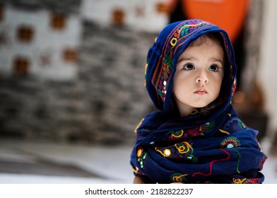 20 months old cute Indian baby girl wrapped in dark blue scarf sitting and looking away innocent