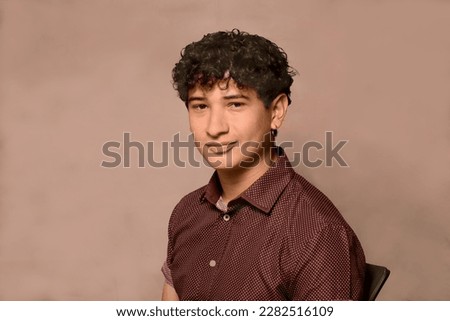 20 year old Hispanic man. Slight smile, wearing a shirt. Light background. Study light.