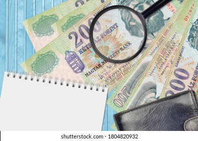 200 ungarische Forint Scheine und Lupe mit schwarzer Handtasche und Notizblock. Konzept der Geldfälschung. Suchen Sie nach Unterschieden in den Details der Geldrechnungen, um Fälschungen aufzudecken