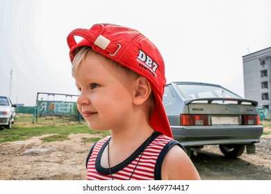 2010.08.15, Obninsk, Russia. A Boy Wearing Red Baseball Cap By The Car, Side View.