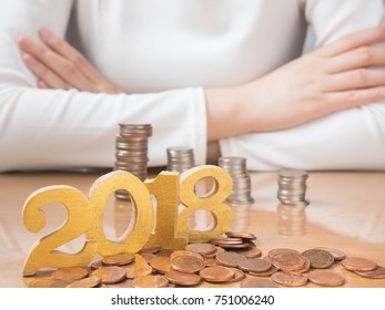 2018 New Year Financial Resolutions And Money Planning Concept. Female In White Shirt W/ Crossed Arm Saving Money For Investment, Travel Or Home W/ Gold Number 2018 And Pile Of Coins On Wood Table.