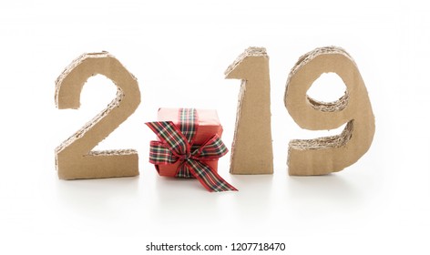 2019, handmade 3D numbers made of reused cardboard paper, with gift box with bow instead of zero, on white background.