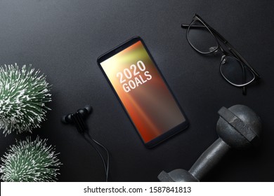 2020 Goals New Year Resolutions Fitness Healthy Goals With Mockup Mobile Phone On Black Table With Dumbbells And Mini Christmas Tree. Mock Up Smartphone.