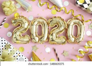 2020, Happy New Year! Golden balloon numbers, shiny streamers, confetti and  wrapped  gift boxes on pastel pink background. Happy 2020 Year. Top view.
