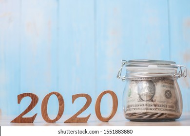 2020 New Year With Money Glass Jar And Wooden Number. Financial, Resolution, Goals, Plan, Action And Saving Concept