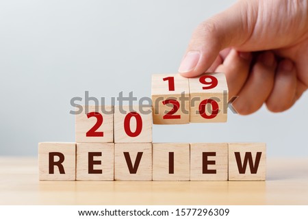 2020 review concept. Hand flip wood cube change year 2019 to 2020 and the word REVIEW on wooden block on wood table