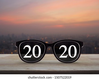 2020 White Text With Black Eye Glasses On Wooden Table Over Blur Of Cityscape On Warm Light Sundown, Business Vision Happy New Year 2020 Concept